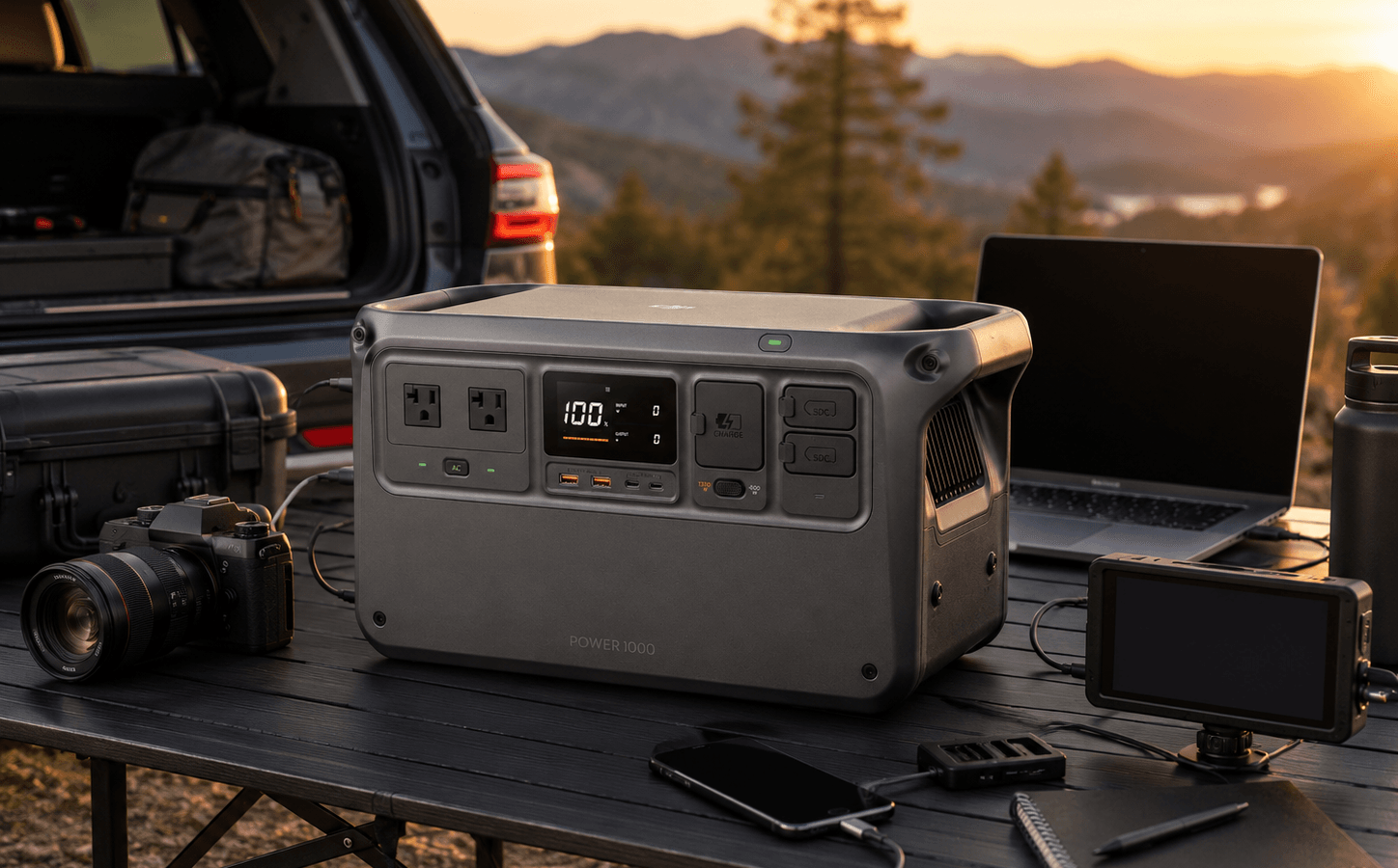 DJI Power 1000 portable power station beside a compact home-office desk with a laptop, router, monitor, phone charger, camera charger, and LED desk lamp.